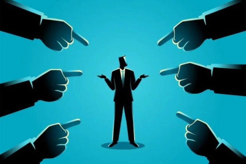 1. Businessman in a suit surrounded by multiple hands pointing at him, illustrating scrutiny or attention in a corporate setting. 2. A businessman stands in the center, with several hands pointing at him, symbolizing focus or criticism in a professional context. 3. A businessman is encircled by hands pointing towards him, representing evaluation or pressure in a business environment.